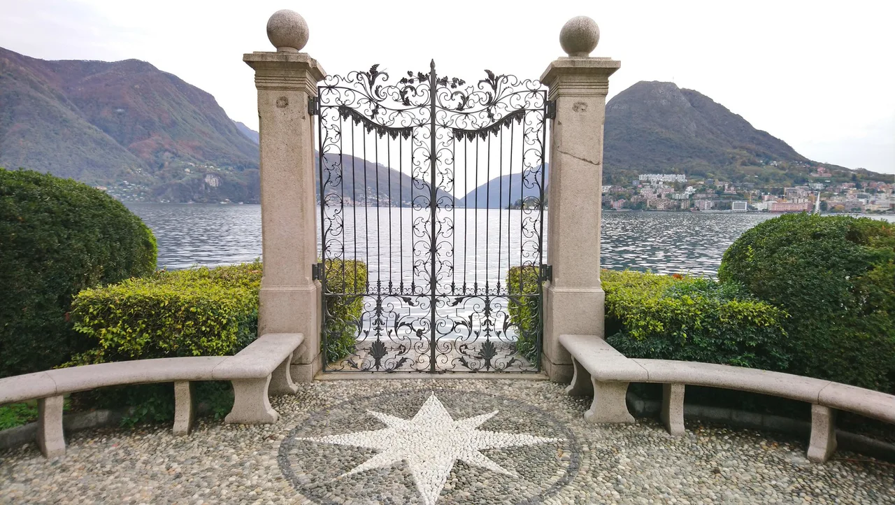 Venue view: the gate and park grounds of Parco Ciani in Lugano, Switzerland, with the lake and surrounding buildings beyond.